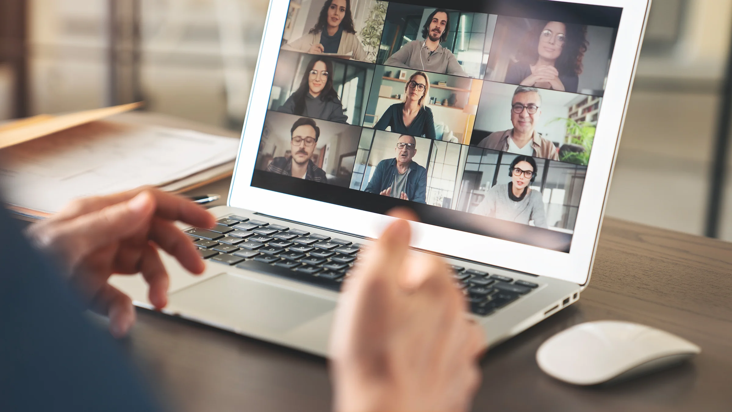 Person am Laptop in einer Videokonferenz mit neun Teilnehmenden im Raster