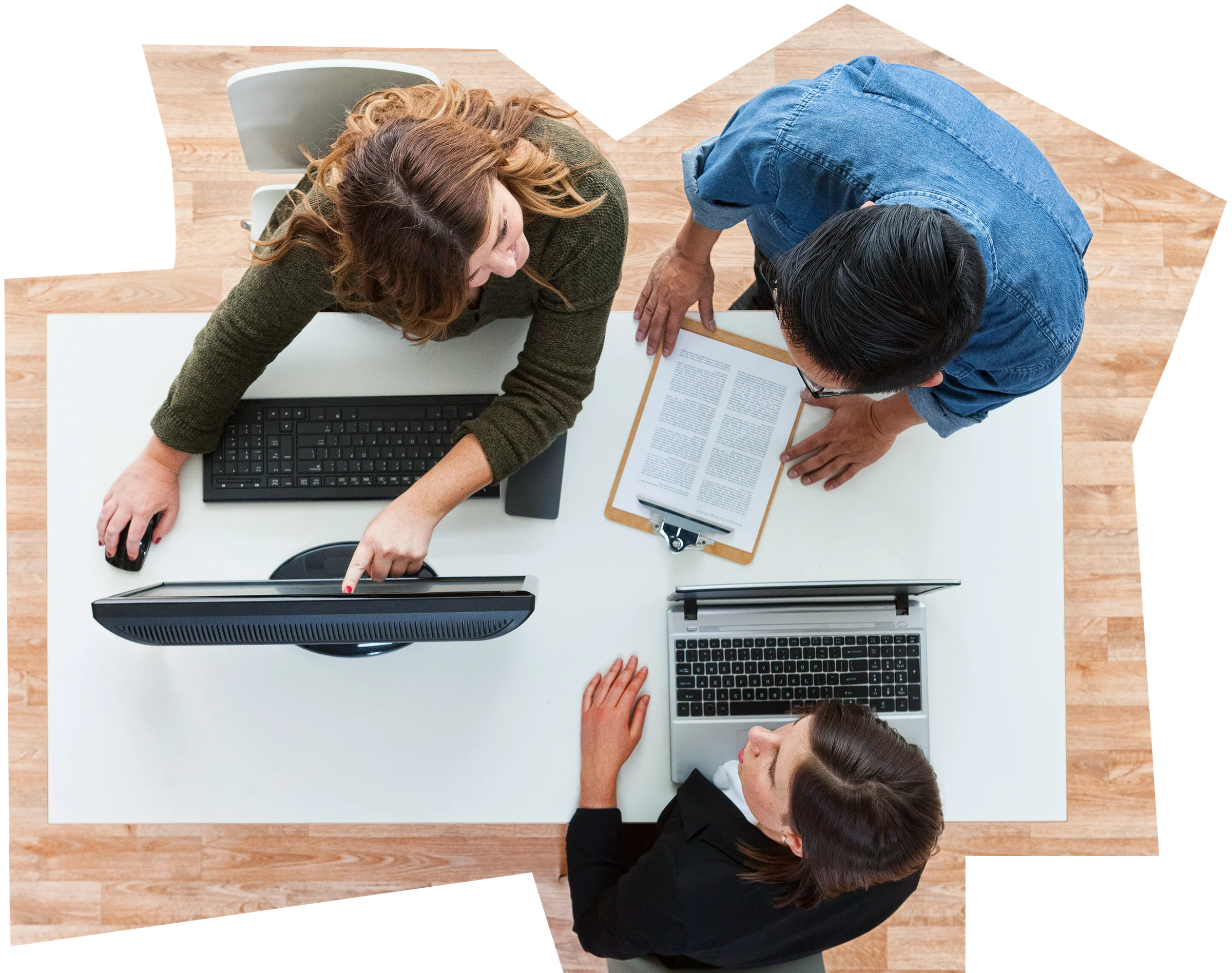 Overhead view of three people at a desk with a monitor, laptop and documents, discussing