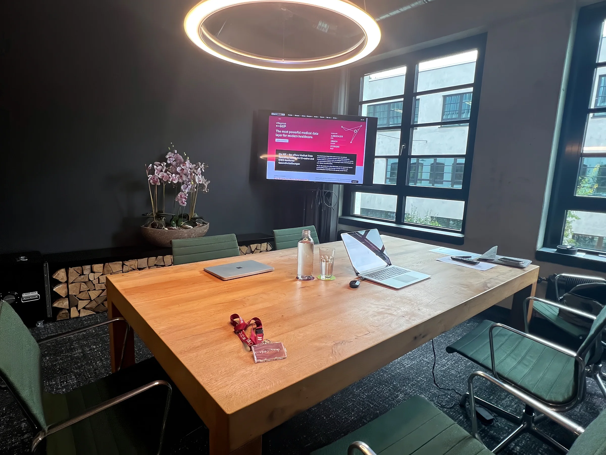 Meeting room with a wooden table and laptops, wall screen showing the vitagroup HIP website